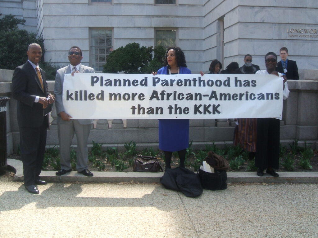 Activists holding a sign which reads "Planned Parenthood has killed more African-Americans than the KKK."